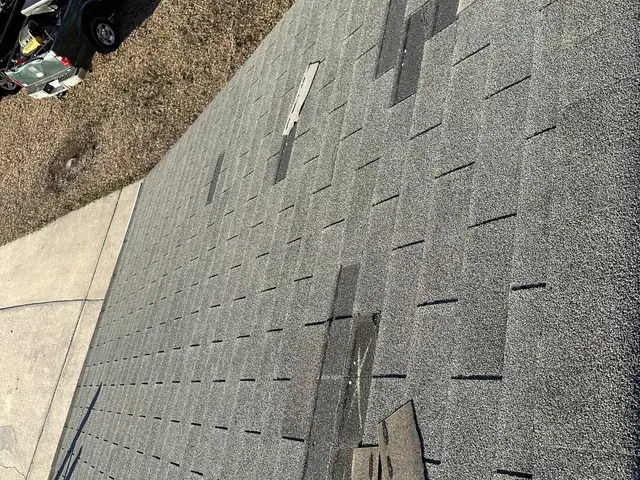 Storm-damaged shingles being replaced across a roof slope